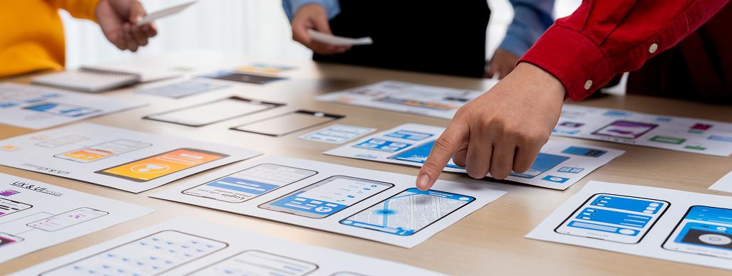 Team reviewing printed UI screens laid out on a table
